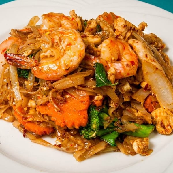 Pad See Ew with shrimp, chicken, broccoli, and carrots on a white plate.