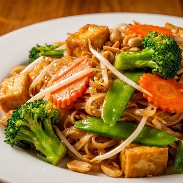 Vegetable Pad Thai with tofu, broccoli, carrots, snow peas, bean sprouts, and peanuts on a white plate.